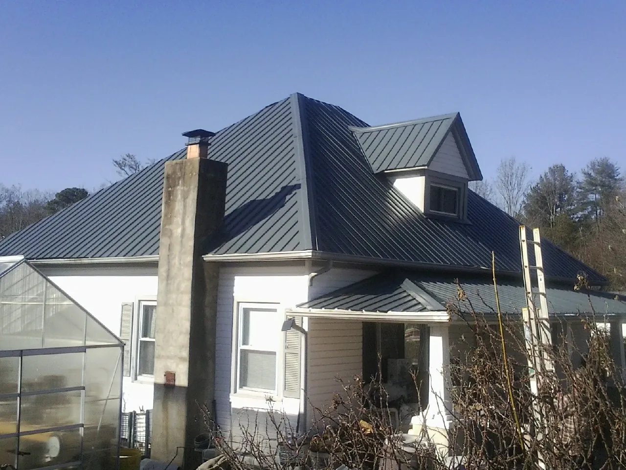 Dark blue standing seam metal roof on a white farmhouse with dormer — Slate & Tile Roof Repair by Roofing Brothers in Conyers