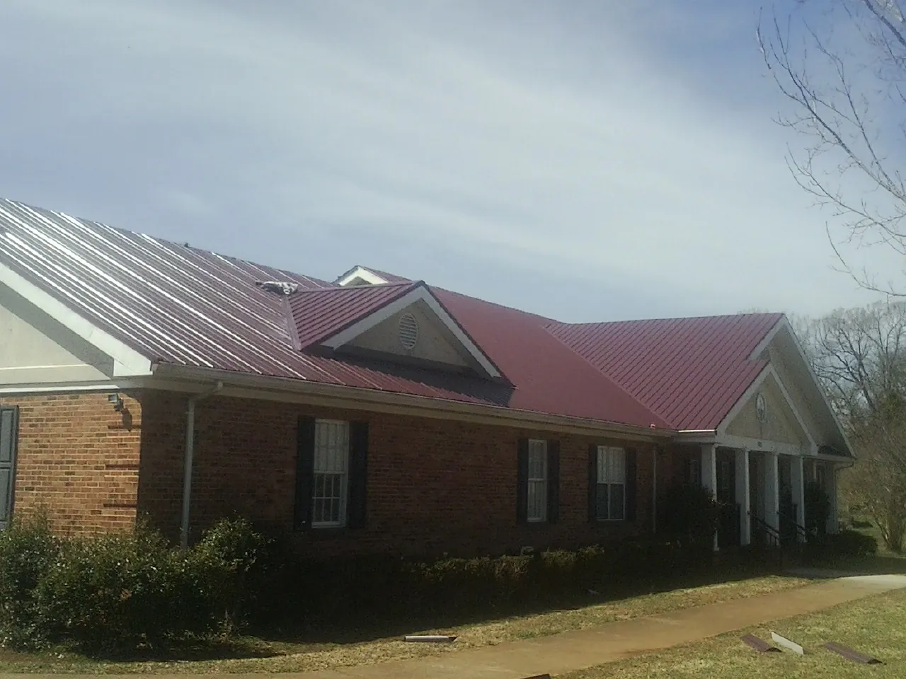 Red metal roof with gabled entries on a long brick building, from a Hail Damage Roof Repair job in Conyers