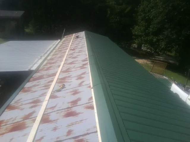 Old rusted panels beside newly installed green metal roofing — Wind Damage Roof Repair by Roofing Brothers in Conyers