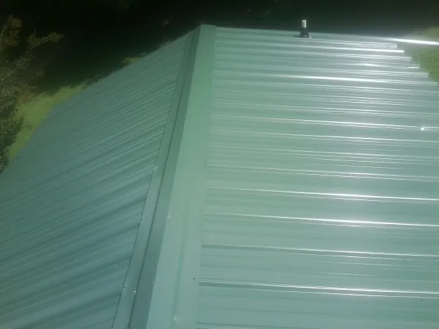 New green metal panels meeting at the ridge of a roof — Flat Roof Repair work by our crew in Conyers