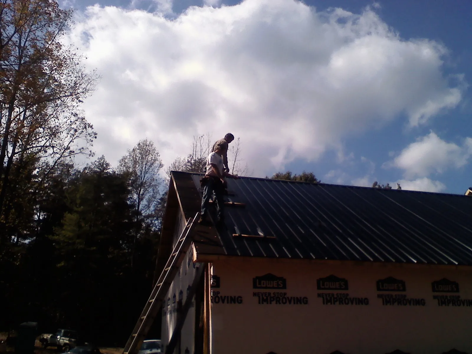 Roofer fastening dark metal panels high against a cloudy sky, from a Roof Inspection job in Conyers