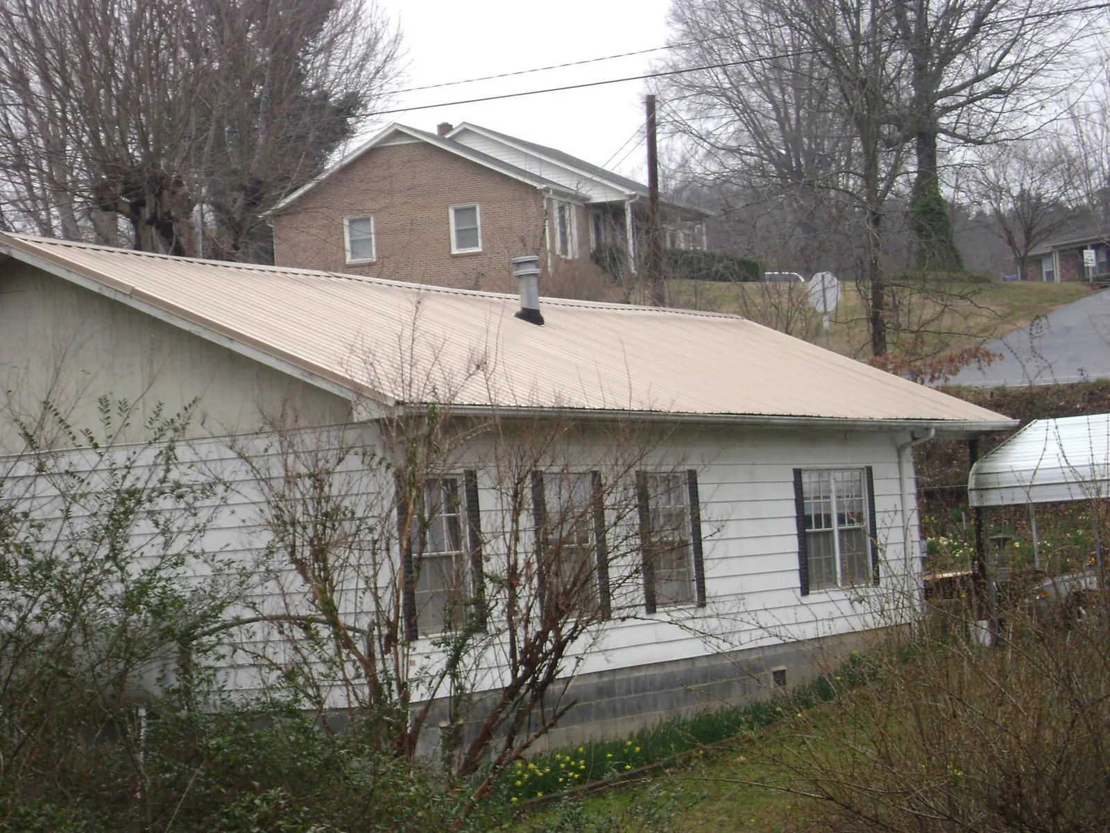 Tan metal roof on a white sided house set into a hillside — Commercial Roofing by Roofing Brothers in Conyers